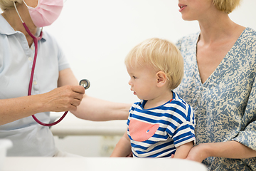 Image showing Infant baby boy child being examined by his pediatrician doctor during a standard medical checkup in presence and comfort of his mother. National public health and childs care care koncept.