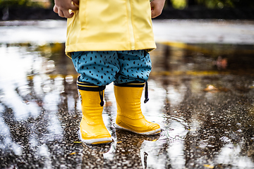 Image showing Small infant boy wearing yellow rubber boots and yellow waterproof raincoat standing in puddle on a overcast rainy day. Child in the rain.