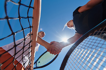 Image showing Two female tennis players shaking hands with smiles on a sunny day, exuding sportsmanship and friendship after a competitive match.