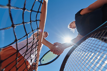 Image showing Two female tennis players shaking hands with smiles on a sunny day, exuding sportsmanship and friendship after a competitive match.