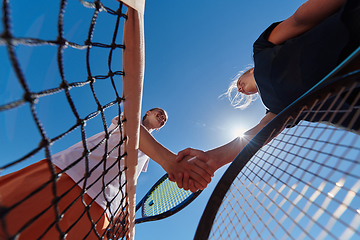 Image showing Two female tennis players shaking hands with smiles on a sunny day, exuding sportsmanship and friendship after a competitive match.