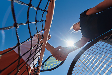 Image showing Two female tennis players shaking hands with smiles on a sunny day, exuding sportsmanship and friendship after a competitive match.