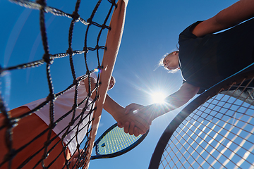 Image showing Two female tennis players shaking hands with smiles on a sunny day, exuding sportsmanship and friendship after a competitive match.