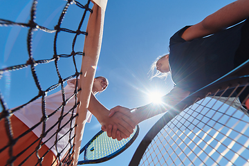 Image showing Two female tennis players shaking hands with smiles on a sunny day, exuding sportsmanship and friendship after a competitive match.