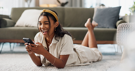 Image showing Woman, phone and portrait with wink, relax and lying on floor for flirting, secret and typing in living room of home. Indian, girl and smartphone on ground for chat, texting or technology with emoji