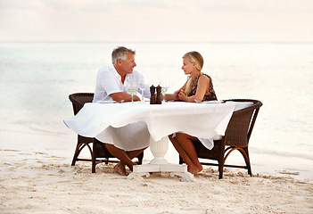 Image showing Beach, dinner and couple with sunset, celebration and romance with anniversary, marriage and tropical island. People, romantic meal or man with woman, ocean and waves with summer holiday and love