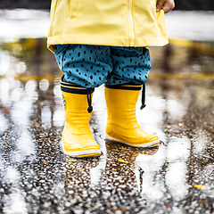 Image showing Small infant boy wearing yellow rubber boots and yellow waterproof raincoat standing in puddle on a overcast rainy day. Child in the rain.