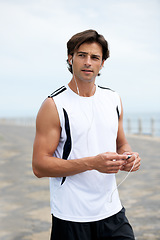 Image showing Man, fitness and earphones to listen to music, podcast and song on run, exercise and cardio. Male athlete, hearing and streaming radio, audio and sound by ocean, outdoors and inspiration for workout