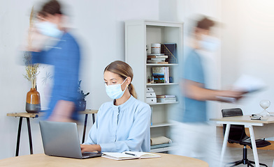 Image showing Business woman, busy office and covid compliance while on laptop and blur of people around her. Employees in the office during coronavirus wearing face mask and working in company after lockdown