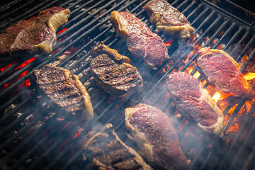 Image showing Rib-eye steaks cooking on flaming grill.