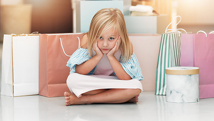 Image showing Bored child, fashion and shopping bags waiting on floor in kids clothing shop, store or boutique with cute girl sitting looking upset. Portrait of kid shopper or customer with sale purchase packages