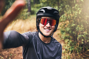 Image showing Man taking a selfie while cycling on a nature trail, wearing a helmet and sunglasses. Portrait of a cyclist on bicycle ride through a park or forest taking a picture smiling and wearing safety gear