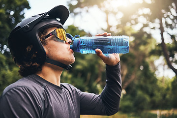 Image showing Cyclist, water and bottle in forest for hydration, with cycling equipment and sunglasses by trees for wellness. Man, drink and sports while exercise, workout or training for fitness outside in woods