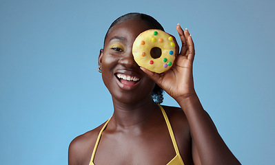 Image showing Beauty, black woman and portrait of donut on face with blue studio wall for happy summer style. Matching, beautiful and fun african american girl with yellow makeup for quirky fashion campaign.