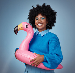 Image showing Portrait of woman in blue with a flamingo and a smile on her face. Happy black woman with inflatable bird rubber ring on hip on blue background. Mockup for trendy, travel and fun for summer vacation