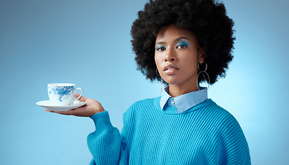 Image showing Tea, fashion and blue with a black woman in makeup on a wall background in studio holding a cup and saucer. Face, portrait and afro with a young female posing for drink, beverage and refreshment