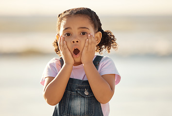 Image showing Wow, children and hands on the face of a girl on the beach looking surprised or shocked outside during summer. Kids, youth and surprise with a little female child feeling shock while outdoor alone