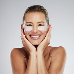 Image showing Skincare, portrait and woman doing face cosmetics, smile and makeup with grey studio background. Facial, mature lady and older female relax, happy and with eye patch, collagen and confidence in skin.