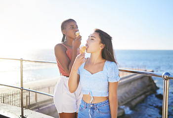 Image showing Girl friends and eating ice cream at the beach together on summer sunshine holiday break in Italy. Carefree and satisfied women relax with tasty Italian dessert cone on European ocean vacation.