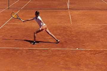 Image showing A young girl showing professional tennis skills in a competitive match on a sunny day, surrounded by the modern aesthetics of a tennis court.