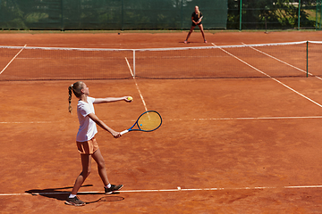 Image showing Young girls in a lively tennis match on a sunny day, demonstrating their skills and enthusiasm on a modern tennis court.