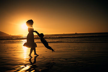 Image showing Sunset, beach and silhouette of a mother and girl playing on the sand while on summer vacation. Family, fun and happy woman swinging her child in nature by the ocean while on holiday in south africa.