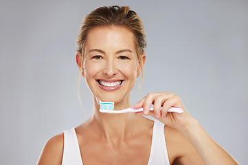 Image showing Teeth, dental and oral hygiene with a woman brushing using a toothbrush and toothpaste in a studio on a gray background. Health, healthcare and face with a female taking care of her mouth and gums