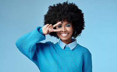 Image showing Young, black woman and shows peace sign with blue studio background, trendy style and afro. Smile, happy and relax African American female, lady or girl influencer with casual fashion and cosmetics.