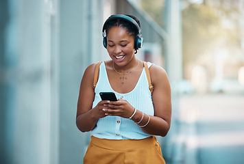 Image showing Urban black woman with smartphone and headphones in city or street walking and listening to music, messaging and typing on chat app. Gen z girl with cellphone with subscription or audio streaming.