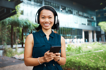 Image showing Asian woman, headphones and phone while streaming music, videos or podcast standing outside on break feeling free and happy on internet. Portrait and smile of happy business female using technology