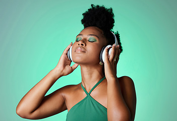 Image showing Black woman in green studio with headphones on, listening to music. Young happy girl with makeup, cosmetics and beauty with wireless earphones streaming a song, podcast or radio for fun and to relax