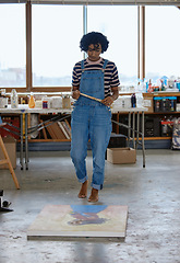 Image showing Art, creative and a woman painting on floor in studio or design school with creativity and paint brush. Artist student from India, painter girl thinking of idea and standing over canvas in classroom.