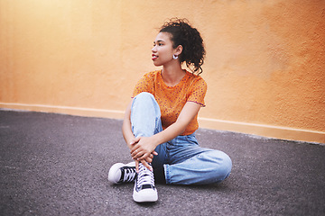 Image showing Fashion, sneakers and young woman on street in the city. Portrait of urban, trendy and black female model against an orange wall background sitting on the road. Style, clothes and girl posing