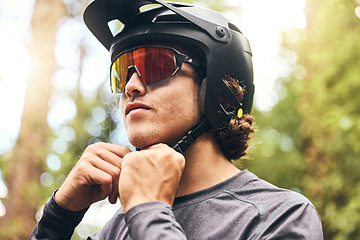 Image showing Fitness, helmet and man cycling in nature on his bicycle outdoors for exercise, training and workout in spring. Sports person riding a bike and fixing headgear on an adventure in the forest or woods