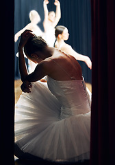 Image showing Dancer thinking backstage at ballet concert or recital while group on theater stage. Girl ballerina waiting on floor of auditorium, anxiety and nerves, for performance in front of audience or crowd