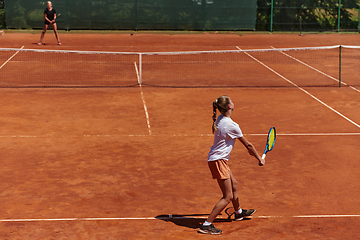 Image showing Young girls in a lively tennis match on a sunny day, demonstrating their skills and enthusiasm on a modern tennis court.