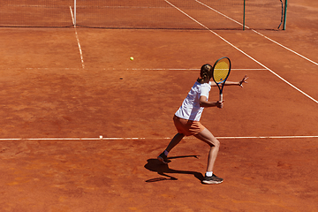 Image showing A young girl showing professional tennis skills in a competitive match on a sunny day, surrounded by the modern aesthetics of a tennis court.