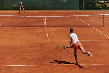 Image showing Young girls in a lively tennis match on a sunny day, demonstrating their skills and enthusiasm on a modern tennis court.