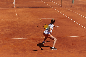 Image showing A young girl showing professional tennis skills in a competitive match on a sunny day, surrounded by the modern aesthetics of a tennis court.