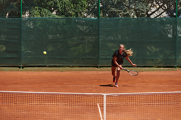 Image showing A young girl showing professional tennis skills in a competitive match on a sunny day, surrounded by the modern aesthetics of a tennis court.