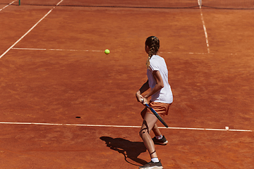 Image showing A young girl showing professional tennis skills in a competitive match on a sunny day, surrounded by the modern aesthetics of a tennis court.