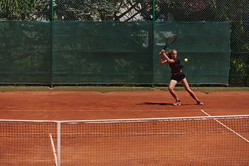 Image showing A young girl showing professional tennis skills in a competitive match on a sunny day, surrounded by the modern aesthetics of a tennis court.