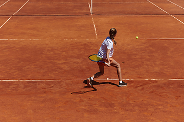 Image showing A young girl showing professional tennis skills in a competitive match on a sunny day, surrounded by the modern aesthetics of a tennis court.