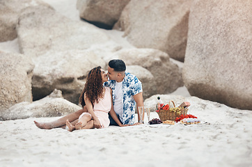 Image showing Couple, beach and love on picnic, kiss and happy together on sand by rock. Man, woman and smile with happiness on face with lips, basket and flowers to relax, vacation and travel in summer in Sydney