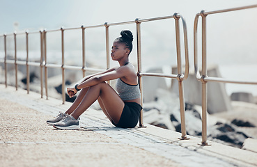 Image showing Runner, ocean and thinking on rest while running in outdoor in the summer by the water. Black woman, athlete and training sitting by the sea to breathe, focus and calm after workout, run or exercise