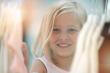 Image showing Fashion, girl and happy shopping child at shopping mall store, boutique or retail shop for discount sales clothes on rack. Happiness, smile and young kid or youth customer looking at fabric product