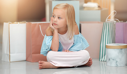 Image showing Child, fashion and shopping bags while looking bored and waiting in a kids clothing shop, store or boutique with cute girl sitting on floor. Little kid shopper or customer with sale purchase packages