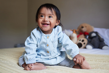 Image showing Baby, down syndrome and special needs child happy with a smile sitting on a bed to relax, be curious and playful in bedroom at home. Cheerful girl with intellectual disability and developmental delay