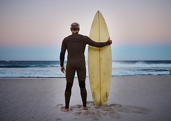 Image showing Surf, sea and sport with a man on the beach with his surfboard looking at the ocean view or horizon at sunset. Health, fitness and sports with a male athlete standing in the sea by water in nature