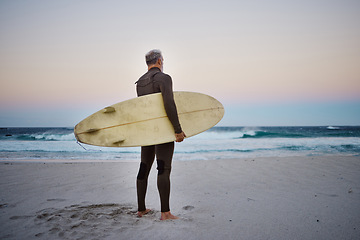 Image showing Surfer, surfboard and senior man on beach at sea waves in during sunset during summer vacation in Hawaii. Professional male athlete rest after training or practice surfing sport outdoor at the ocean